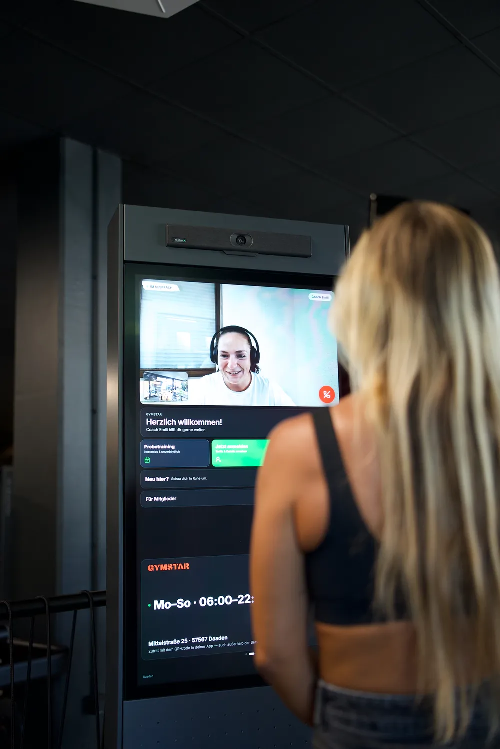 Live-Videogespräch am Gymmy Terminal: Coach mit Headset auf dem Bildschirm, Mitglied davor